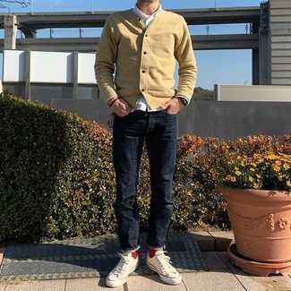 Men's Outfits 2021: Go for a straightforward yet casually dapper option by pairing a beige cardigan and navy jeans. If you wish to immediately dial down this look with one single piece, why not complete your outfit with a pair of white canvas low top sneakers?