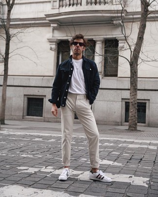 Navy Denim Jacket Outfits For Men: This combination of a navy denim jacket and beige chinos will allow you to flex your skills in menswear styling even on lazy days. Complete your look with white and black leather low top sneakers to instantly step up the street cred of this getup.