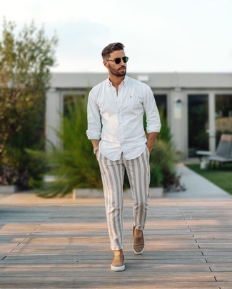 White and Navy Vertical Striped Chinos Outfits: Teaming a white long sleeve shirt with white and navy vertical striped chinos is an on-point idea for a laid-back and cool look. Tan canvas slip-on sneakers are a welcome companion for your outfit.
