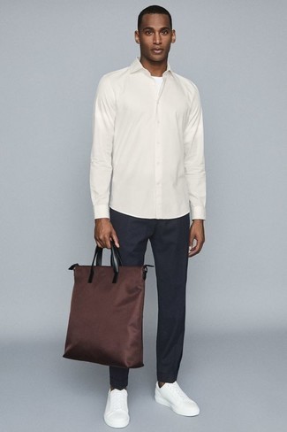 Brown Canvas Tote Bag Outfits For Men: A white long sleeve shirt and a brown canvas tote bag are a wonderful outfit formula to add to your menswear arsenal. Want to dress it up on the shoe front? Complete this getup with white leather low top sneakers.