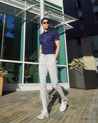 1200+ Casual Hot Weather Outfits For Men: Parade your skills in men's fashion in this casual combo of a navy polo and grey chinos. Let your outfit coordination prowess really shine by completing your look with a pair of white canvas high top sneakers.