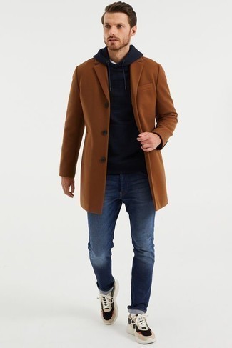 500+ Chill Weather Outfits For Men: A brown overcoat and navy jeans are essential in any gentleman's great wardrobe. When this getup is too much, play it down by wearing a pair of beige athletic shoes.
