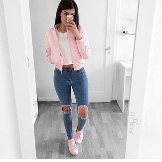 A pink bomber jacket and blue ripped skinny jeans are robust players in any girl's wardrobe. Complement this ensemble with pink low top sneakers and the whole outfit will come together.