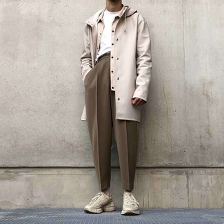 Raincoat Outfits For Men: You'll be surprised at how extremely easy it is for any gentleman to get dressed like this. Just a raincoat matched with brown chinos. Take an otherwise classic look in a more informal direction by slipping into beige athletic shoes.