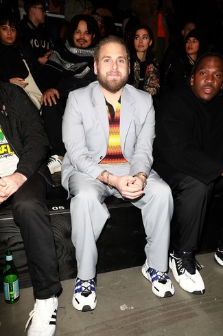 Jonah Hill wearing Grey Suit, Multi colored Horizontal Striped Polo, White and Navy Athletic Shoes, Gold Watch