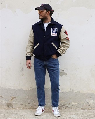 White and Red Canvas High Top Sneakers Outfits For Men: This pairing of a navy varsity jacket and blue jeans will allow you to show off your skills in men's fashion even on lazy days. Up the cool of this outfit by finishing with a pair of white and red canvas high top sneakers.
