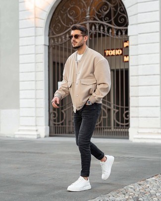 Charcoal Ripped Jeans Outfits For Men: Wear a beige varsity jacket with charcoal ripped jeans for both stylish and easy-to-achieve look. To give your outfit a more polished vibe, why not throw in white leather low top sneakers?