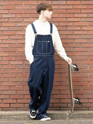 Navy Denim Overalls Outfits For Men: A big yes to this relaxed combo of a white hoodie and navy denim overalls! Let's make a bit more effort now and add black and white canvas low top sneakers to your outfit.